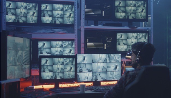 An image of a man sitting in a chair with many computer screens in front of him